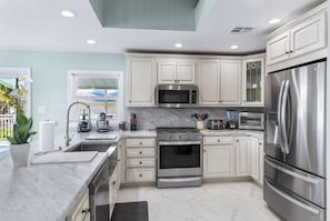 A modern kitchen with white cabinetry, stainless steel appliances, and a marble countertop.