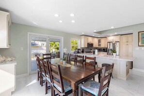 Une cuisine spacieuse avec des meubles blancs, un îlot central et un coin repas comprenant des chaises et une table en bois.