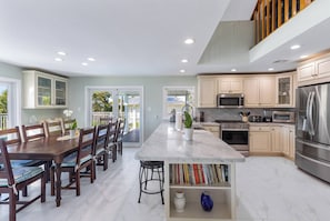A modern kitchen with a central island, stainless steel appliances, and a dining area with wooden chairs.