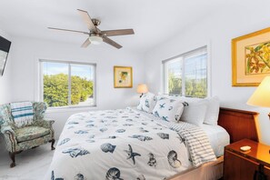 Une chambre à coucher comprenant un lit, une chaise, un ventilateur de plafond, deux fenêtres et une lampe.