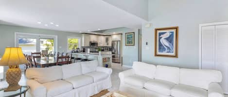A spacious living area with white sofas, a coffee table, and a dining area with chairs and a table.
