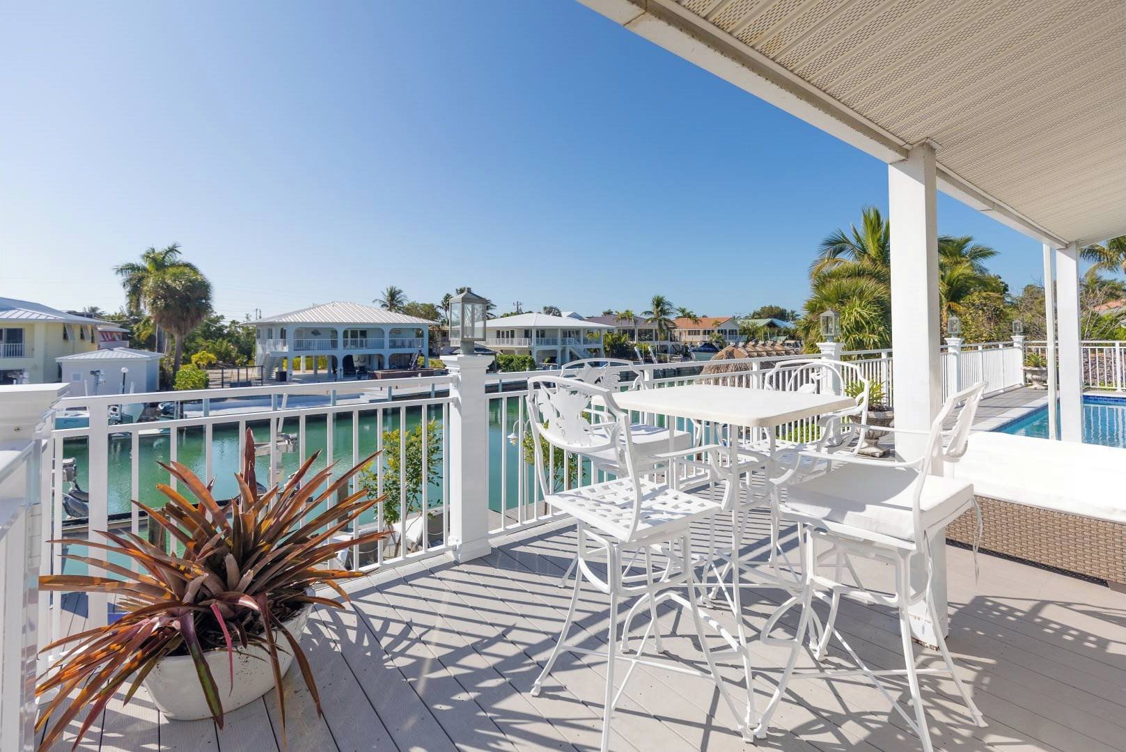 A balcony with white furniture, a pool, and a view of other buildings.
