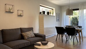 Una sala de estar moderna con un sofá marrón oscuro, una mesa redonda y una zona de comedor con una mesa de madera y sillas negras.