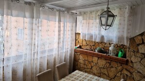 Un comedor con una mesa y sillas, una pared de piedra, un farol colgante y una ventana con cortinas de flores.