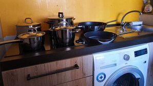 Una cocina con ollas y sartenes de acero inoxidable, un lavamanos y una lavadora.