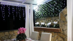Un comedor con una mesa dispuesta para dos, una planta en maceta y una pared de piedra con una planta trepadora.