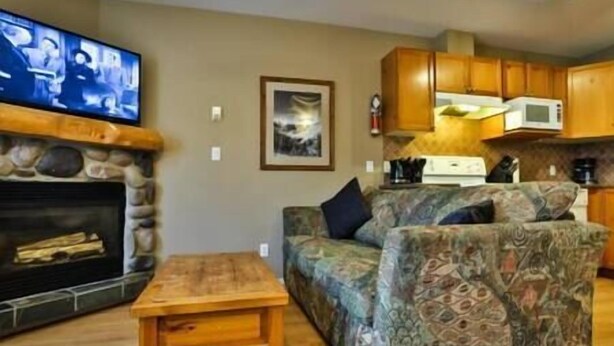 A living room with a fireplace, a sofa, a coffee table, and a television. - 2 BDR Townhouse / Mountain Views / Patio (Fernie)