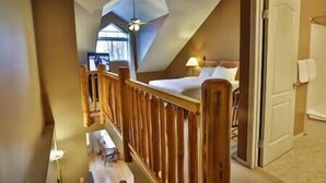 A bedroom with a sloped ceiling, a wooden railing, a bed, and a nightstand. - 2 BDR Townhouse / Mountain Views / Patio (Fernie)