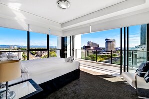 Een moderne hotelkamer met een groot bed, een bureau en een stoel. Er is uitzicht op de stad door grote ramen.