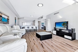 A modern living room with a flat-screen TV, a sofa, and a coffee table. - 3BR Apartment Hinterland Views - Sierra Grand (Broadbeach)