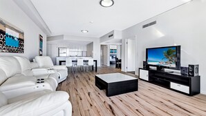 Una sala de estar moderna con un sofá blanco, una mesa de centro y un televisor sobre un mueble negro.