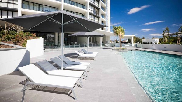 A swimming pool area with lounge chairs and umbrellas, surrounded by a modern building.