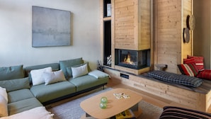 A cozy living room with a green sofa, a wooden fireplace, and a wall-mounted abstract painting. - New 8 Pax Apartment, Parking, Near Slopes (Les Belleville)