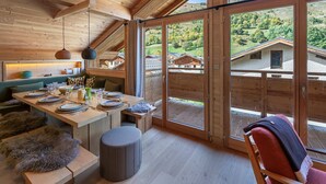 A wooden interior with a dining area, a bench, and a view of houses through large windows. - New 8 Pax Apartment, Parking, Near Slopes (Les Belleville)