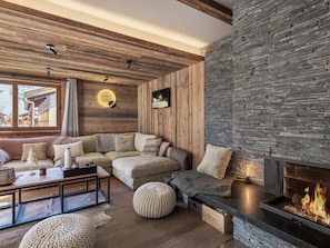 A cozy living room with a wooden ceiling, stone wall, and a fireplace.