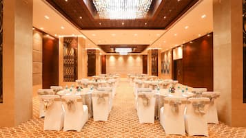 A conference room with a patterned carpet, white chairs with bows, tables with water bottles, and a large chandelier.