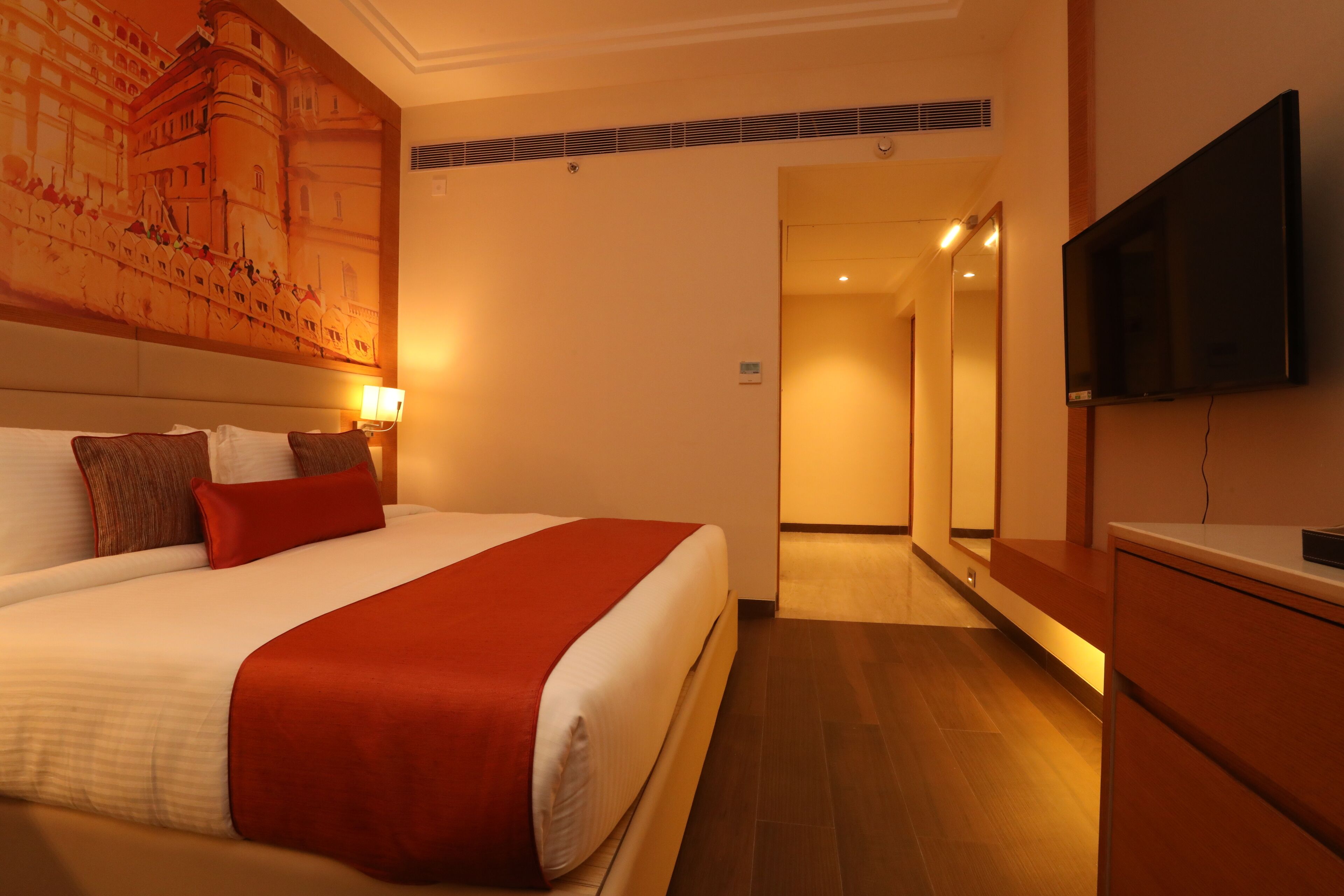 A hotel room with a large bed, a flat-screen TV, a wooden cabinet, and a mural on the wall.