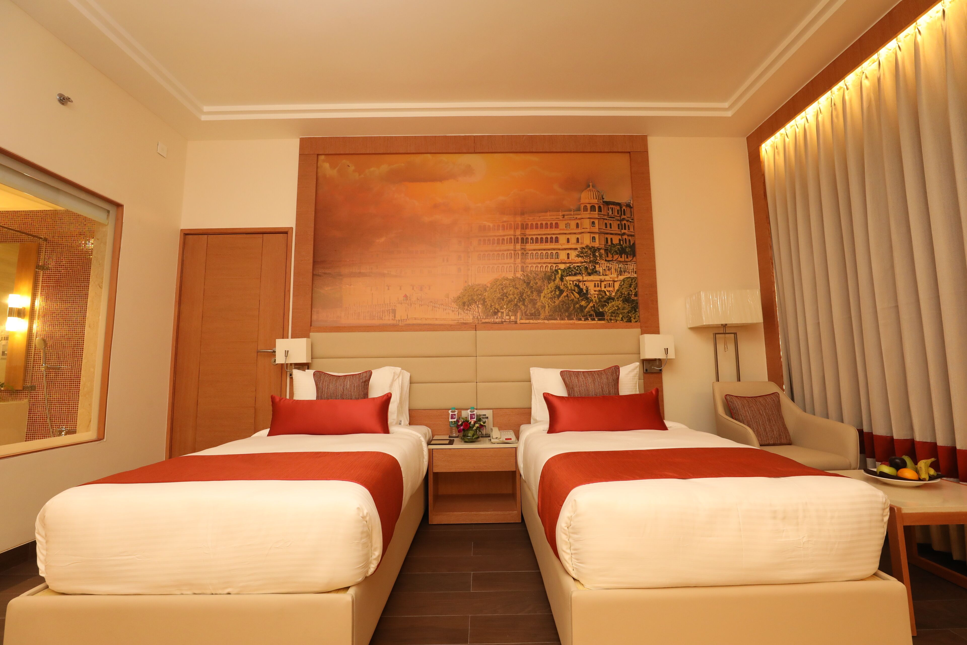 A hotel room with two beds, a painting of a building, a nightstand with toiletries, and a view of a cityscape.