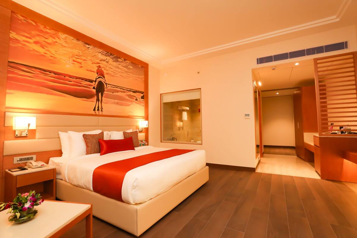 A hotel room with a large bed, a nightstand, a bedside table with a phone, a mirror, and a bathroom with a sink and mirror.
