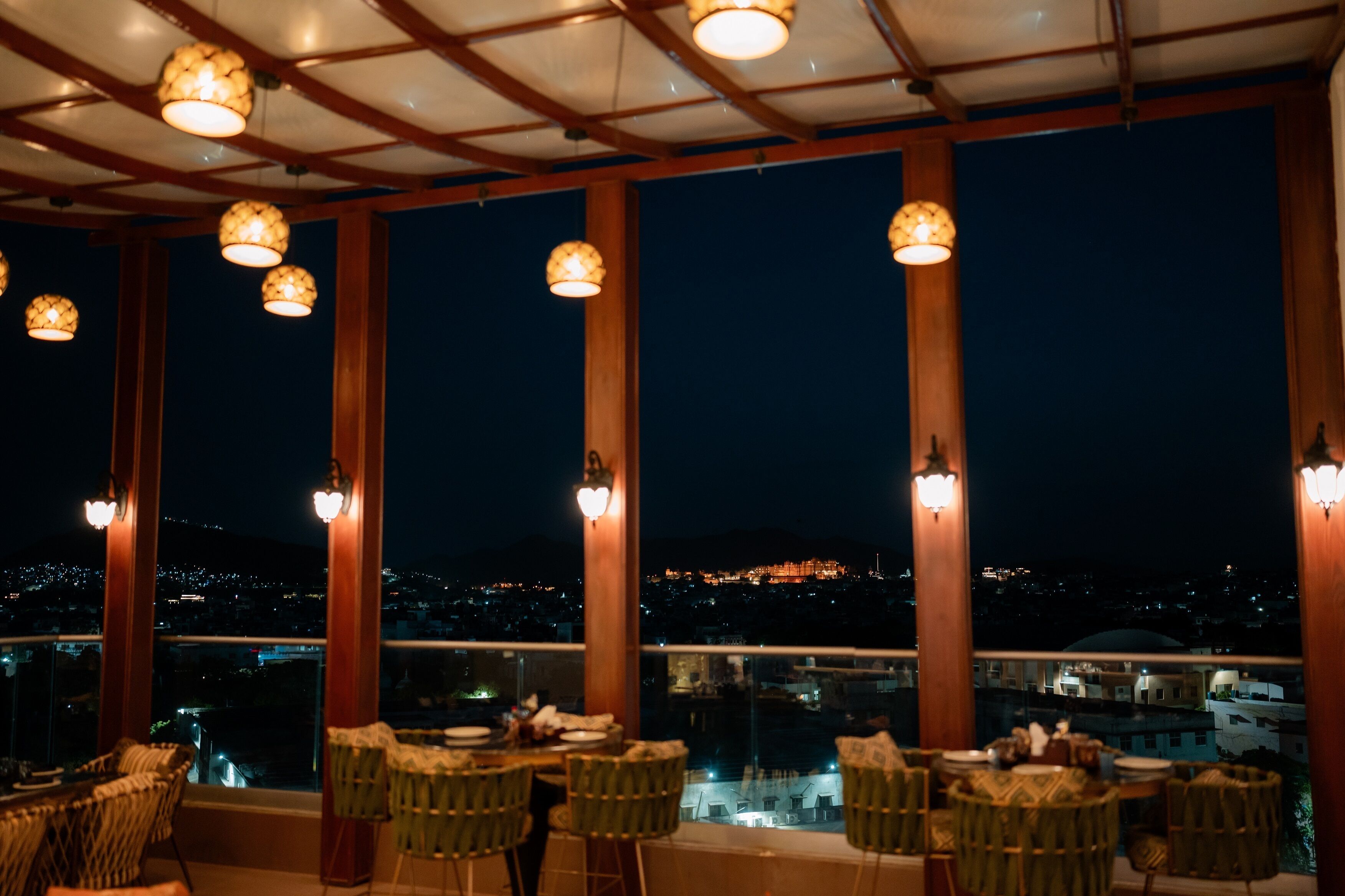 A restaurant with tables and chairs, large windows, and hanging lights.