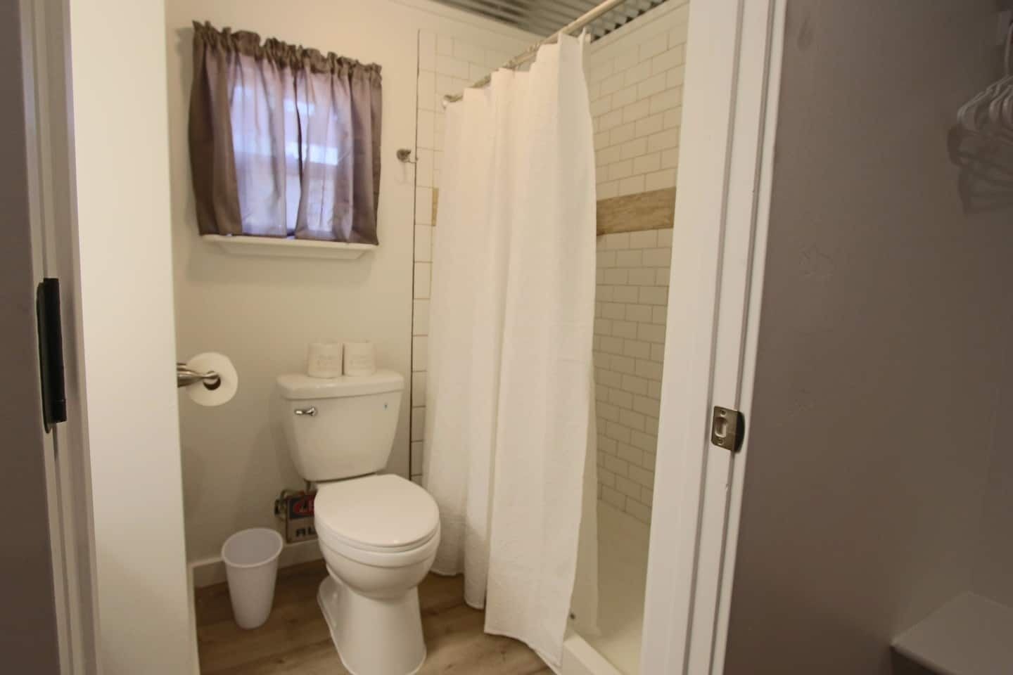 Un baño con inodoro, cortina de ducha y ventana con cortinas.