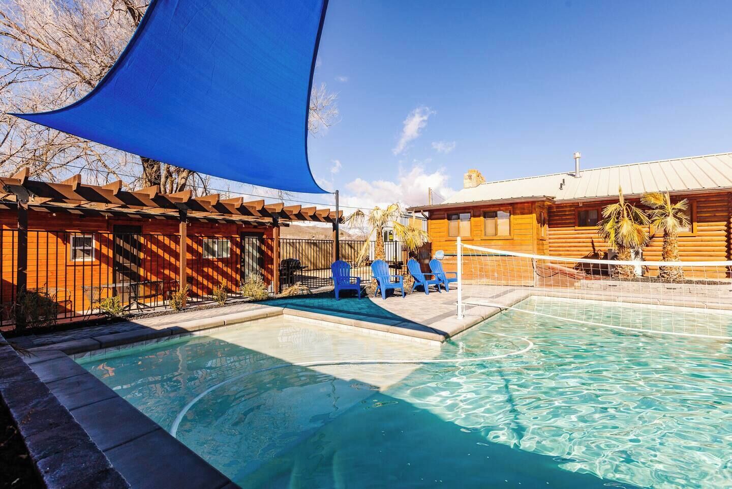 Ein Poolbereich mit Holzterrasse, blauen Stühlen und einem blauen Sonnensegel.