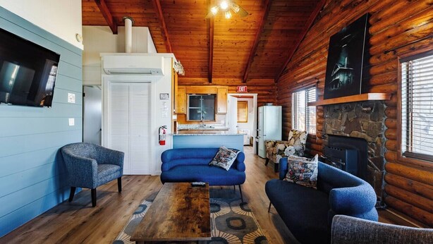 A cozy cabin interior with a living area featuring a blue sofa, two armchairs, a wooden coffee table, and a stone fireplace. - Area 51 | Private Micro Pool-Resort | Pets OK (Hurricane)