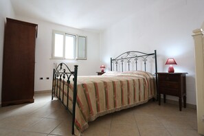 A bedroom with a bed, two bedside tables, a wooden wardrobe, a window, and a mirror.