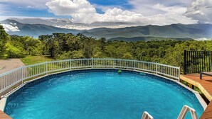 A swimming pool with a wooden deck and a white railing, surrounded by lush greenery and mountains in the background. - 10 min to Soaky mntns & shoping, private backyard (Sevierville)