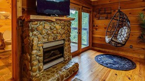 A cozy cabin interior with a stone fireplace, a television mounted above it, and a hanging chair. - 10 min to Soaky mntns & shoping, private backyard (Sevierville)