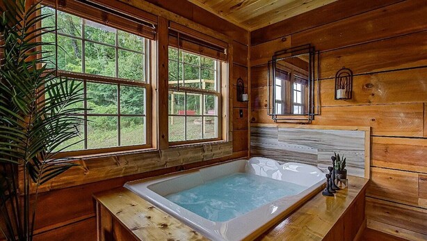 A wooden cabin interior with a large bathtub, wooden walls, and large windows overlooking greenery. - 10 min to Soaky mntns & shoping, private backyard (Sevierville)