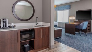 A modern hotel room with a kitchenette, a large mirror, a flat-screen TV, a desk, and a comfortable chair. - Hampton Inn & Suites Cedar Park North Austin (Cedar Park)