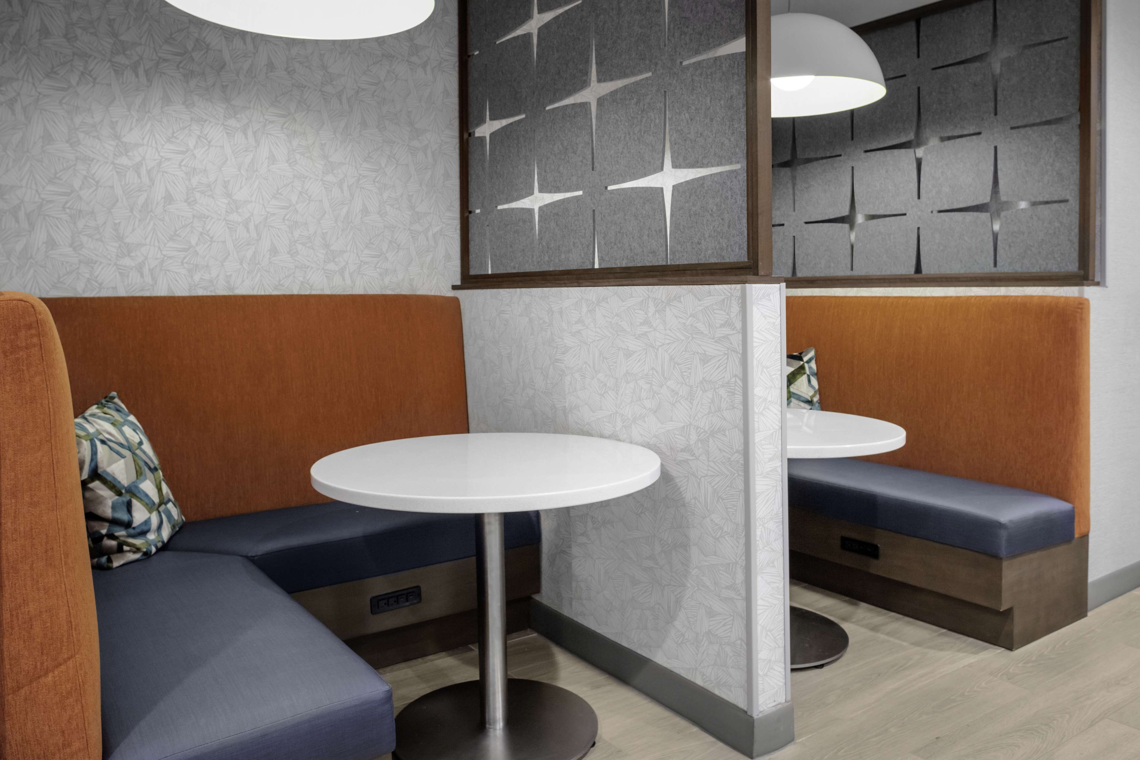 A modern interior with a seating area featuring blue and orange upholstered benches, a round white table, and a decorative wall panel with geometric patterns.