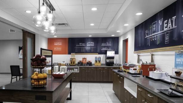 A modern kitchen area with a central island, a coffee station, and a large chalkboard with menu items. - Hampton Inn & Suites Cedar Park North Austin (Cedar Park)
