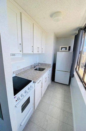 A compact kitchen with white cabinets, a granite countertop, a sink, a stove, and a microwave.
