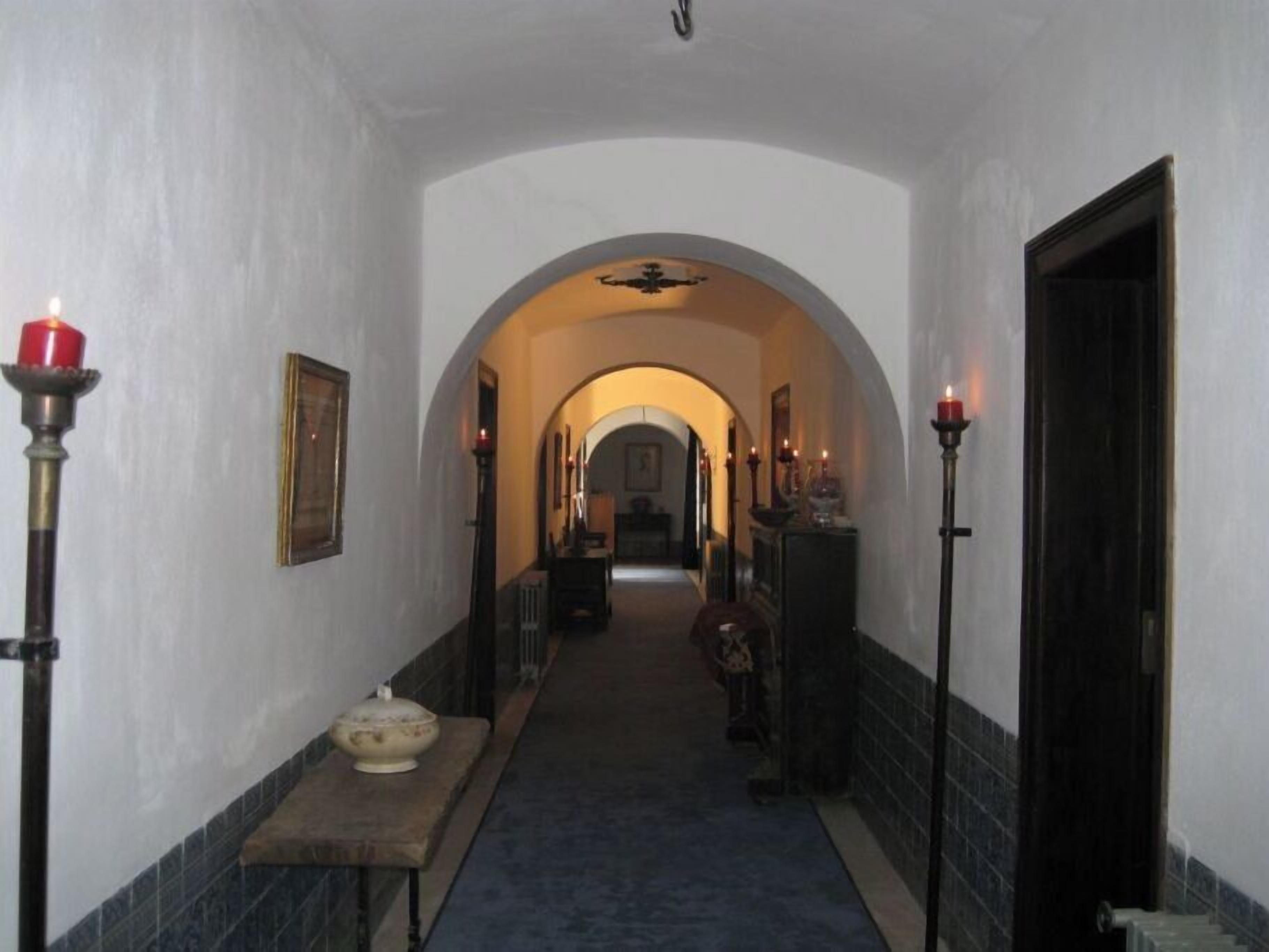 A narrow hallway with an arched ceiling, flanked by candlelit sconces and a central table with a bowl.