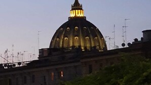 A large, illuminated dome structure with a central spire, surrounded by buildings and antennas. - St. Peter's Private Room (Roma)