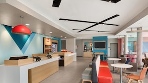 A modern hotel lobby with a reception desk, seating area, and a kitchen in the background.