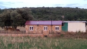 Un edificio de piedra rústico con techo rojo, un cobertizo verde y un campo cercado en primer plano.