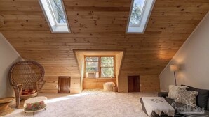 Ein gemütliches Dachzimmer mit Holzbalken, geneigter Decke und zwei Dachfenstern.