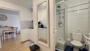 A compact kitchen with a dining area, a white-framed mirror, and a shower with a glass door.