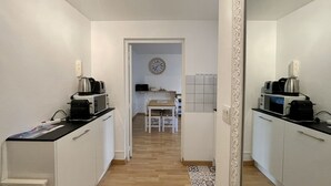 A narrow hallway with a kitchen area at the end, featuring a microwave, kettle, and toaster on a counter.