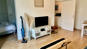 A modern living room with a TV, a wooden bench, a decorative vase, and a vacuum cleaner.