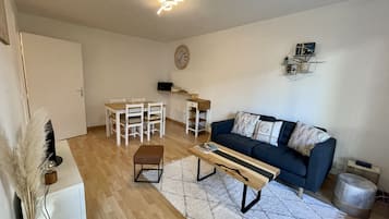 En stue med en mørkeblå sofa, et træ sofabord, en hvid måtte, et spisebord med stole og et lille sidebord.