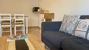 A living room with a grey sofa, a white chair with cushions, a wooden coffee table, and a wall-mounted shelf with a television and decorative items.
