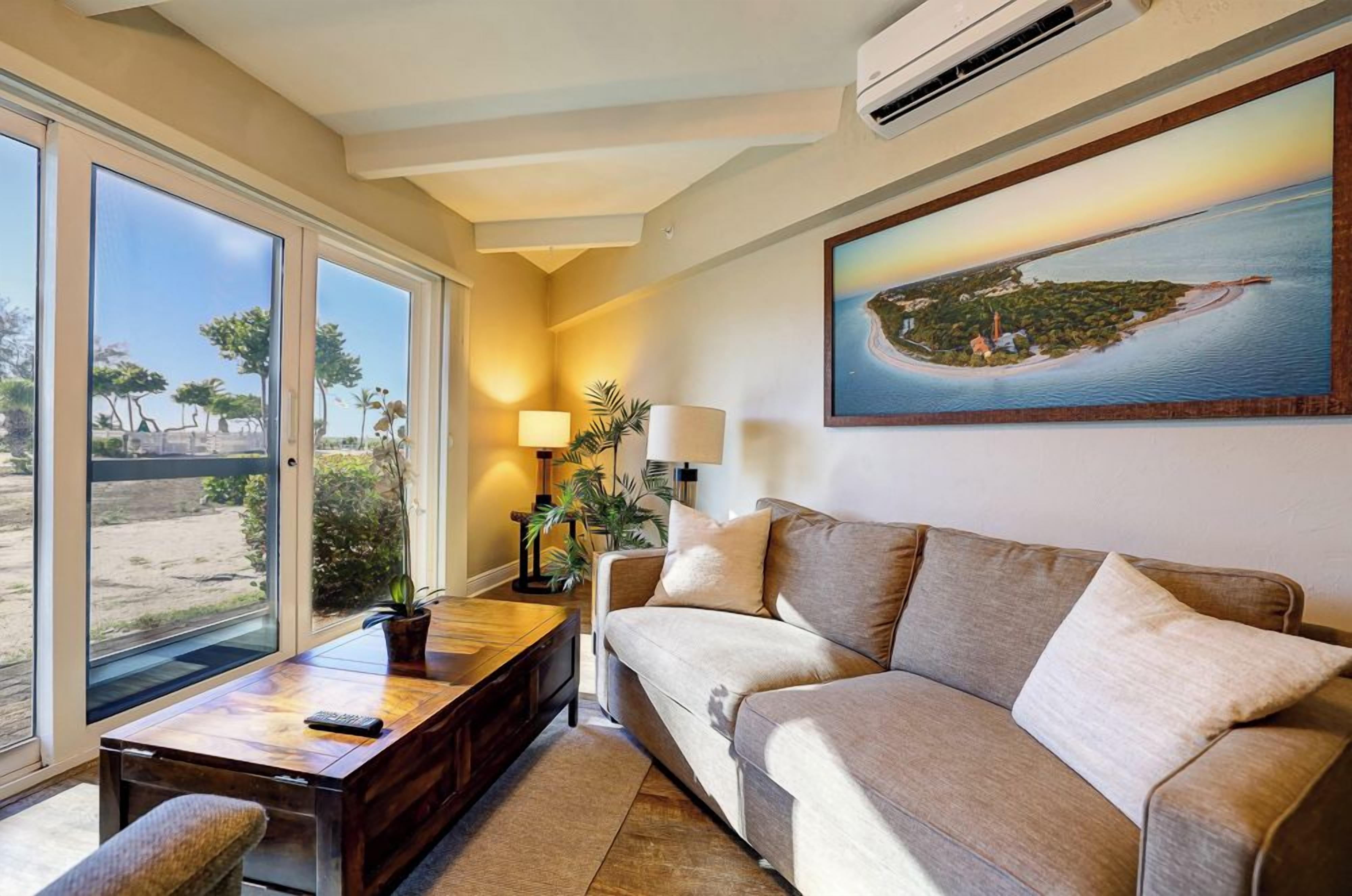 A living room with a sofa, coffee table, and a painting of a coastal scene.
