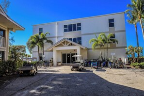 A modern building with a central entrance, surrounded by palm trees and bicycles. - Kimball Lodge #244 - Charming 1brm, 1 and a half bath, Beachside condo! (Sanibel)