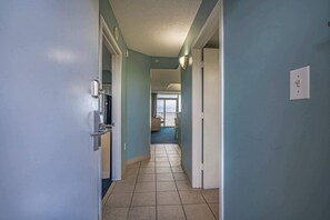 A hallway with a tiled floor, a door on the left, and a window at the end.