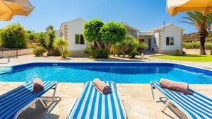 A swimming pool with lounge chairs and umbrellas, surrounded by greenery and a building. - Villa Amorosa in Neo Chorio (Neo Chorio)