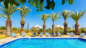 A swimming pool with blue water, surrounded by palm trees and lounge chairs with umbrellas. - Villa Amorosa in Neo Chorio (Neo Chorio)